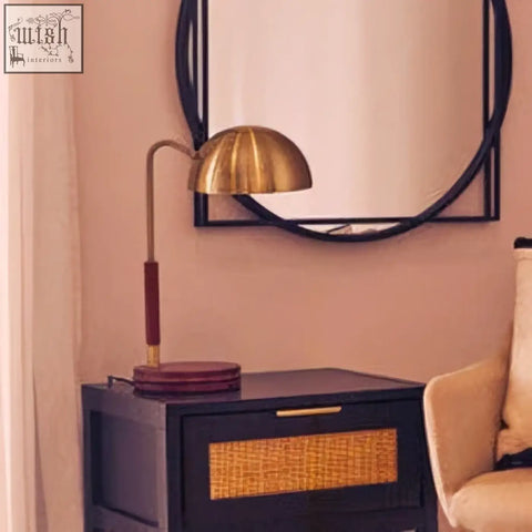 A dark navy nightstand with woven wicker drawer front next to a sydnee brass finish task lamp with wood base