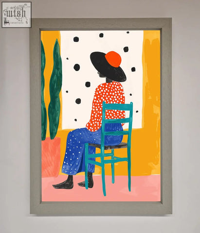 A vibrant seat framed poster with a figure in an orange polka-dot top on a teal chair in a light gray frame
