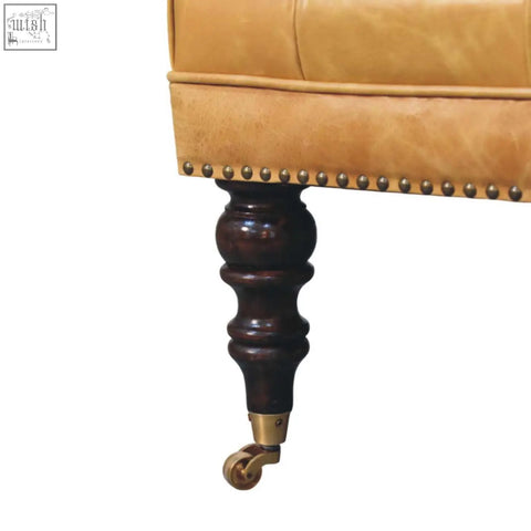 Tan leather upholstered ottoman with brass nailhead trim and dark wood legs with brass caster wheels