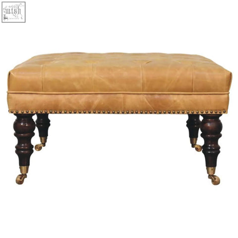 Tan leather upholstered ottoman with tufted top dark wood legs and brass casters for stylish living room seating