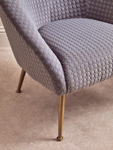 A plush tania grey occasional chair with light gray upholstery, bubble texture, and slender gold tone metal legs