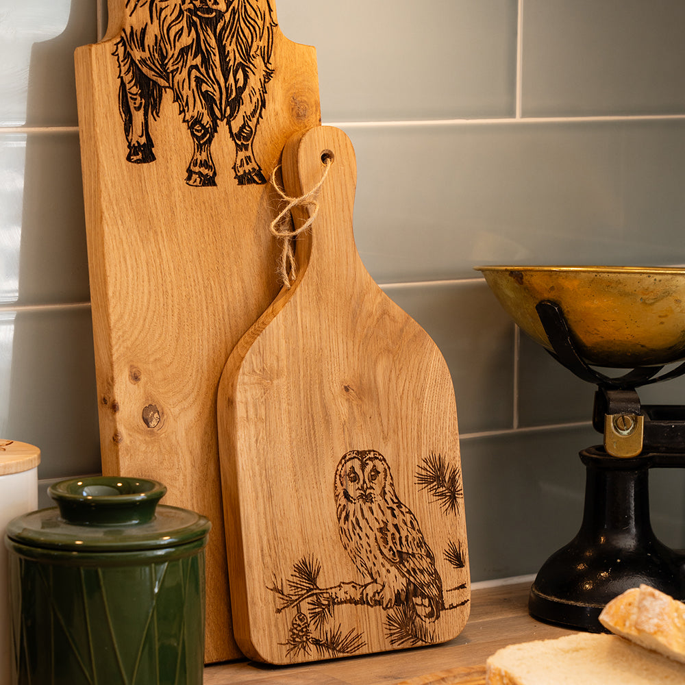 Light wooden oak paddle cutting board engraved with a detailed tawny owl perched on pine branches