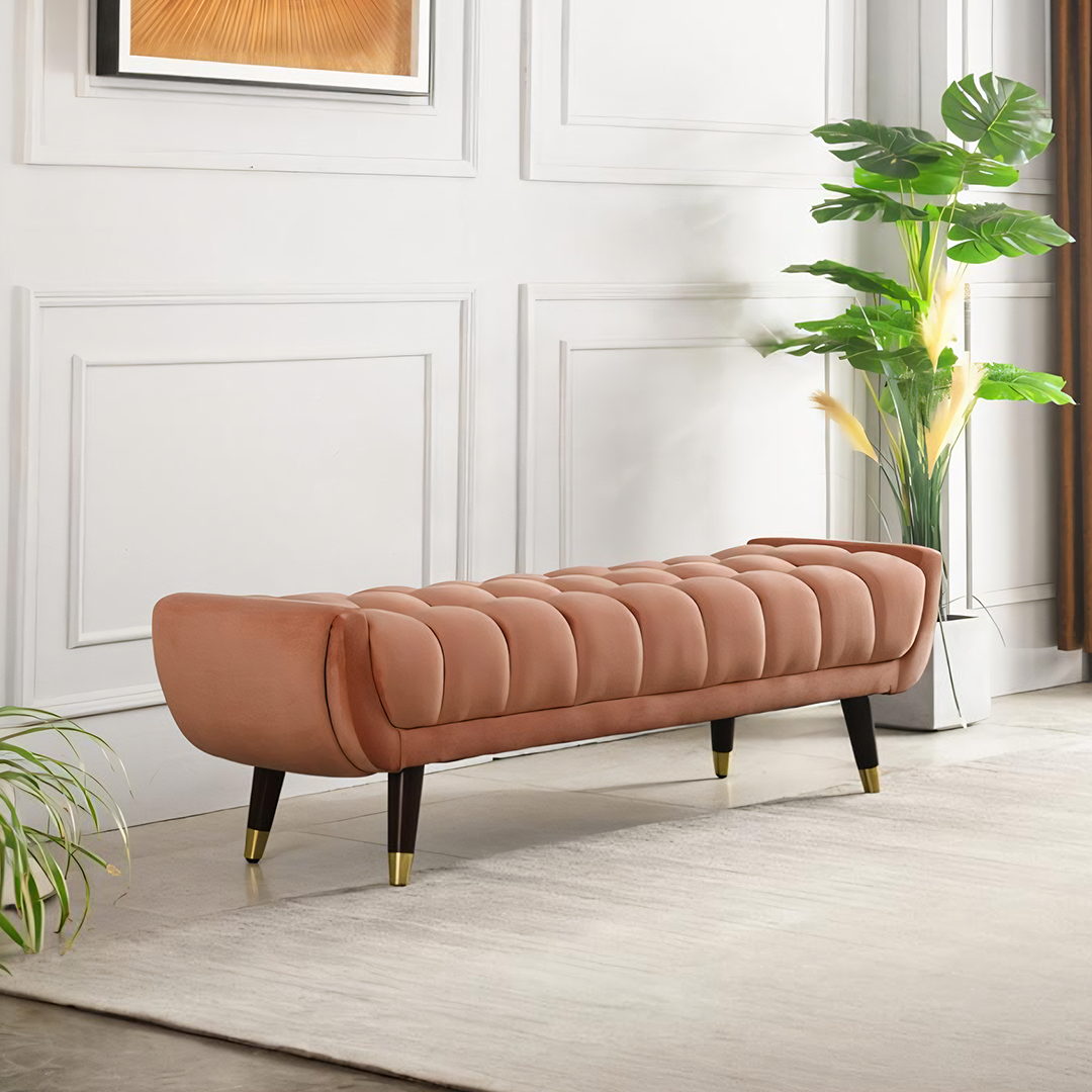 A sleek tb15 orange bench with rose gold velvet tufted upholstery and dark wooden legs with brass accents