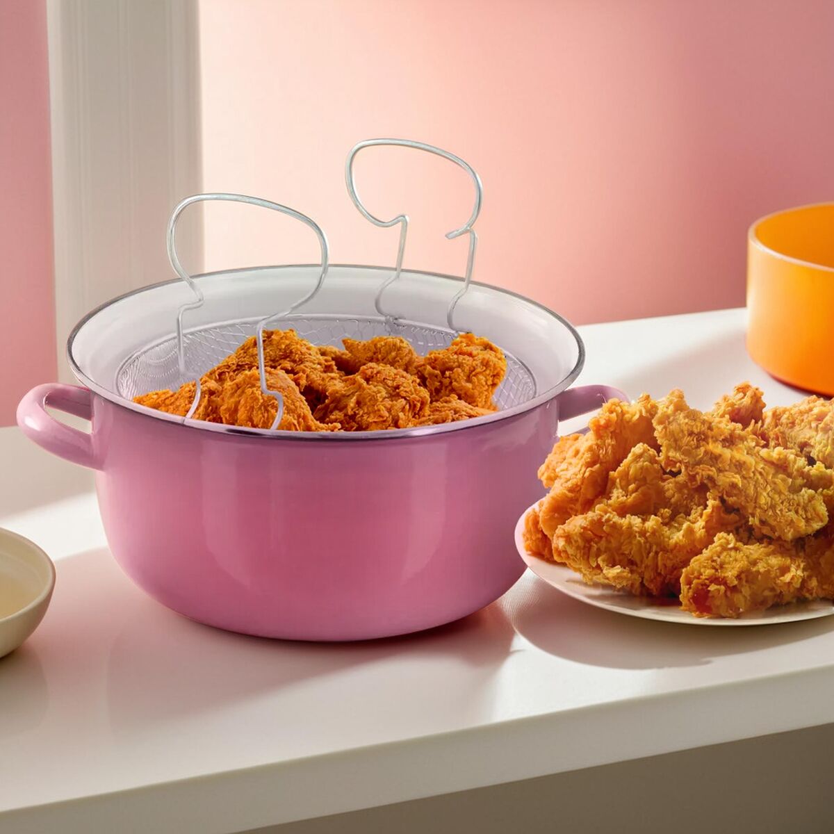 Pink enamel telo pink deep fryer with wire mesh strainer holding golden brown fried chicken pieces