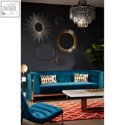 Teal velvet sofa with tufted back and gold-tone metal legs next to templar brass finish wall mirror with brass finish frame
