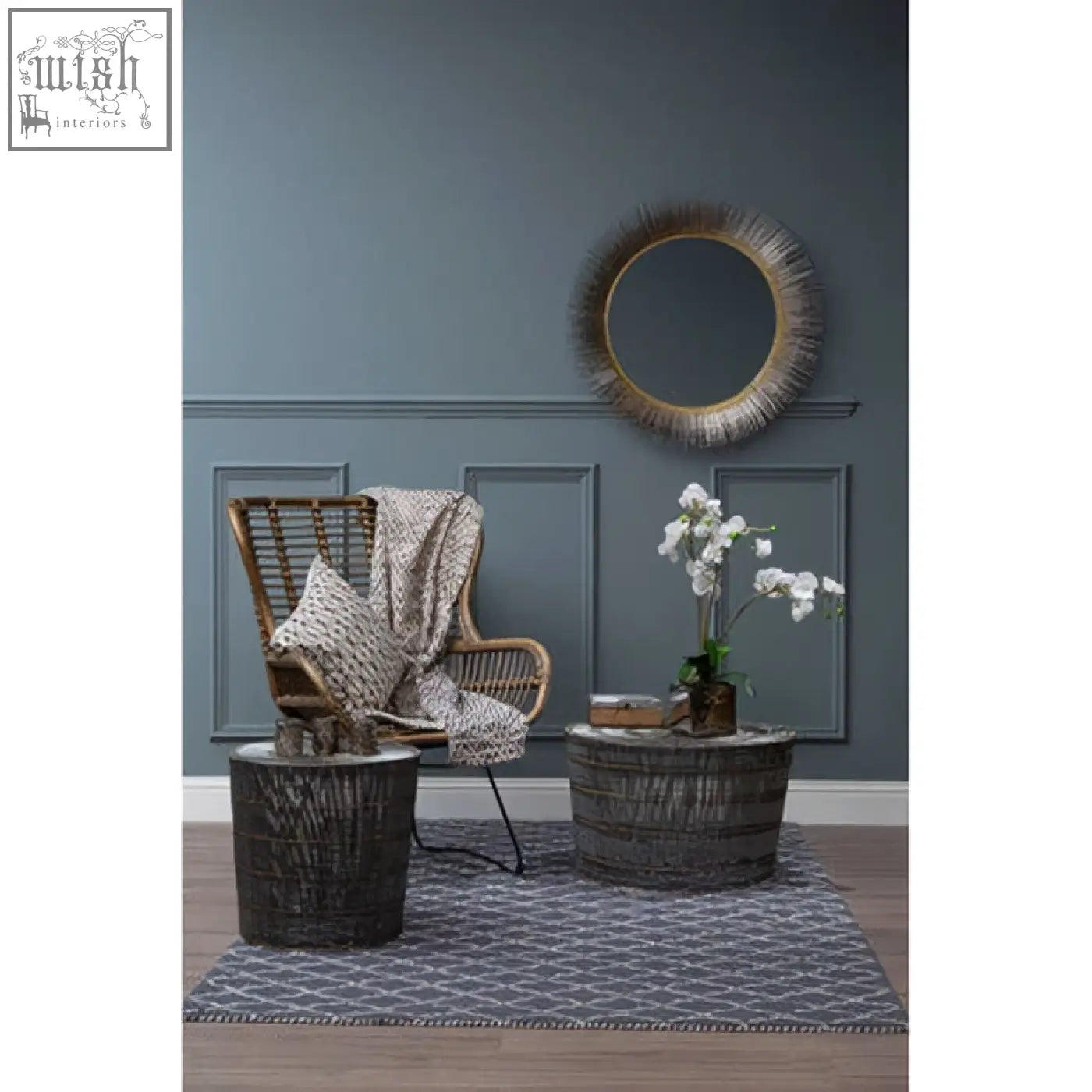 Woven rattan armchair with gray throw blanket next to templar brass finish wall mirror with brass finish frame