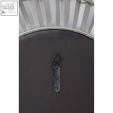 The back of a round dark gray metal-framed sunburst wall mirror with decorative fan edges and a hanging bracket