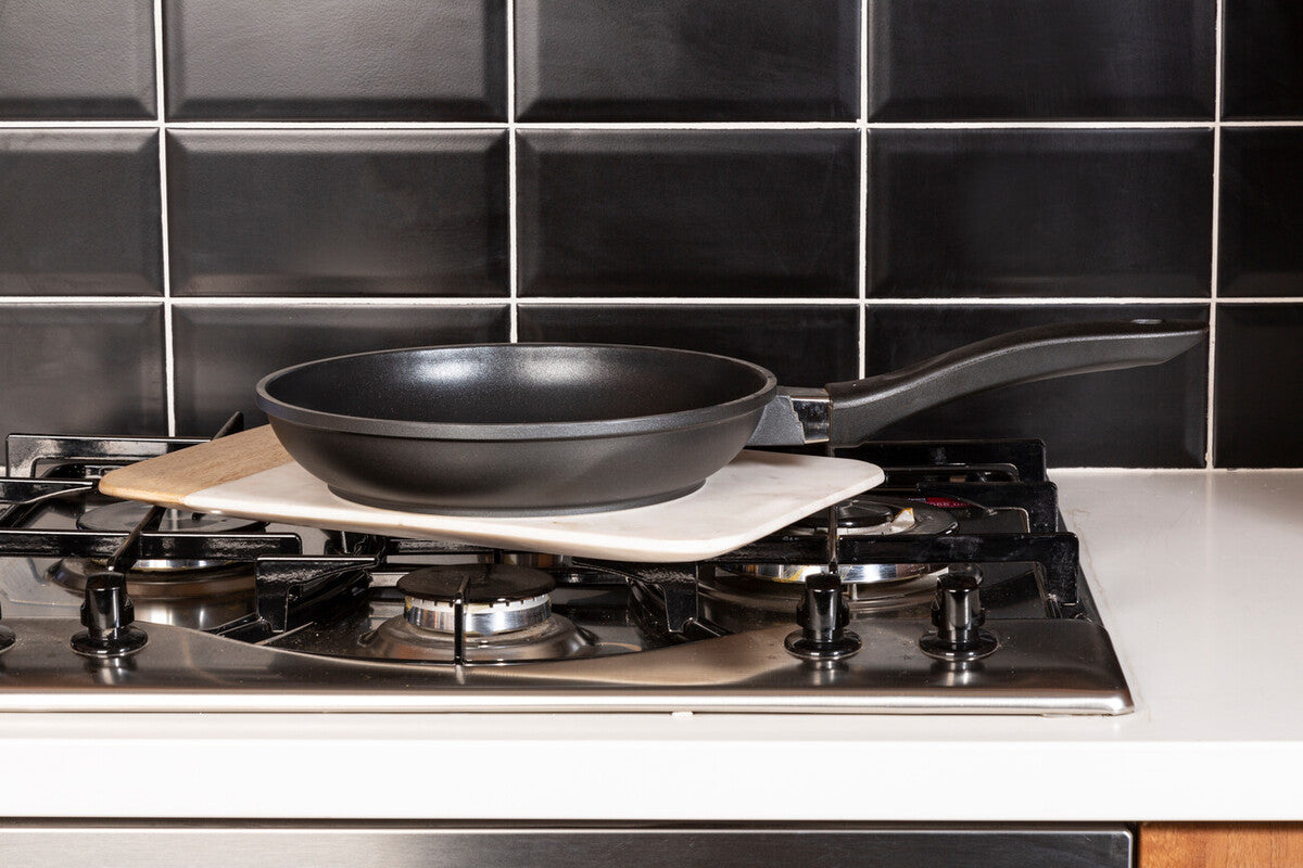 Tenzo 24cm non-stick frying pan black with long handle resting on a heat-resistant mat over a gas stove