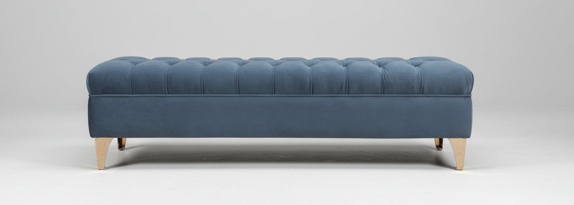 The barton foot stool is a blue tufted velvet storage bench with light wood legs perfect for extra seating or storage