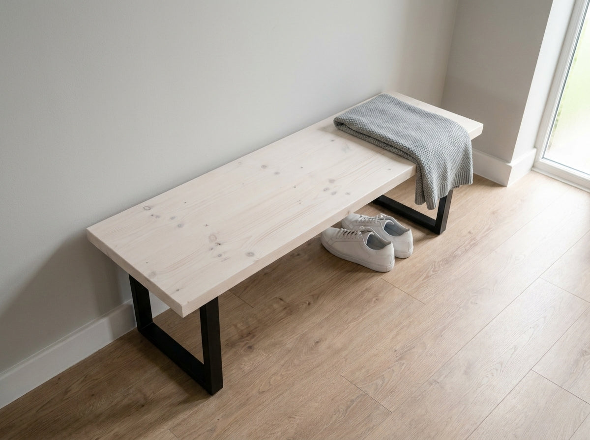 The bruton bench white is a minimalist white wooden bench with black metal legs and a folded gray knit blanket on top