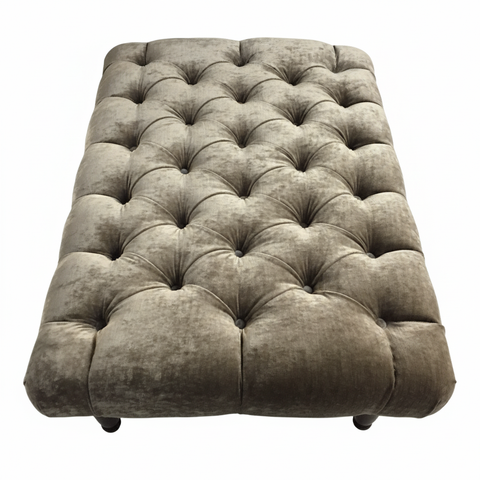 The chester foot stool is a tufted gray velvet ottoman with buttoned design and dark wooden legs