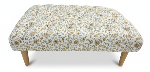 The Chester Foot Stool is a tufted ottoman with white and gold floral fabric and slender wooden legs
