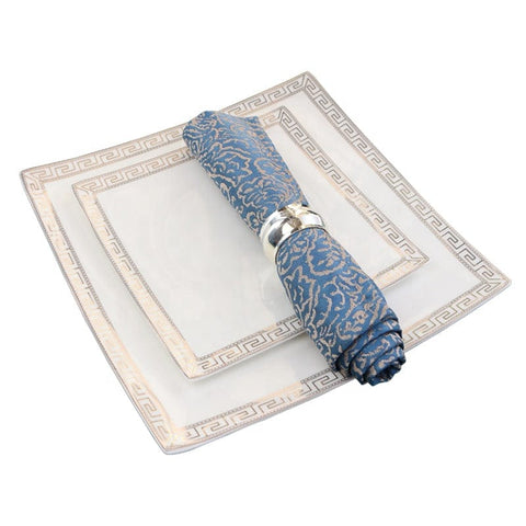 The glamour bone china dinner set features white square plates with greek key border and a blue patterned napkin rolled with a silver ring