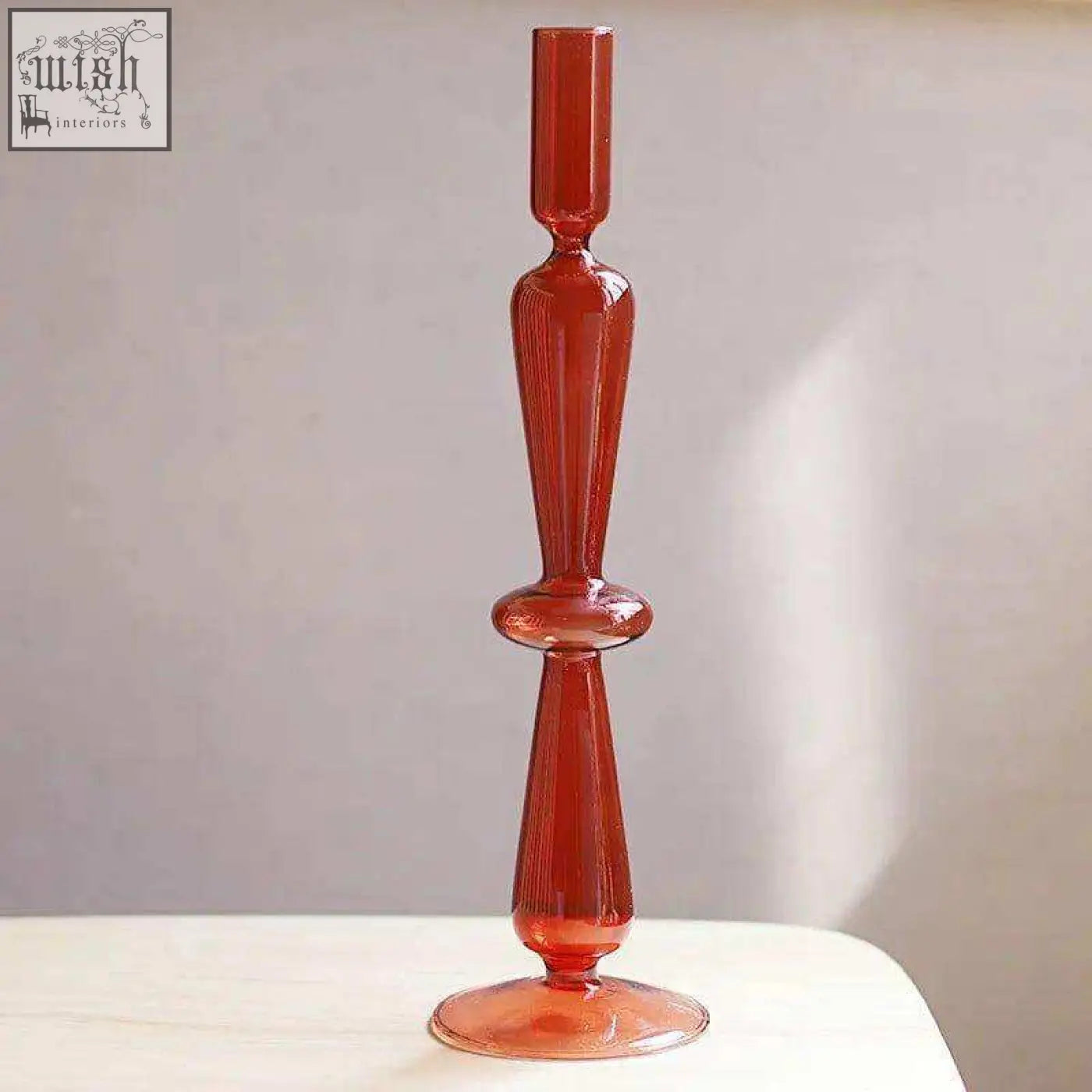 A tall translucent amber glass candle holder with a slender stem and decorative bulbous midsection