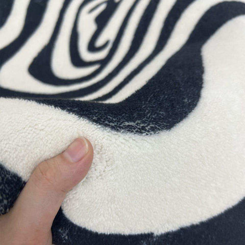 The illusion rug is a plush soft blanket with a bold black and white zebra stripe pattern perfect for cozy spaces