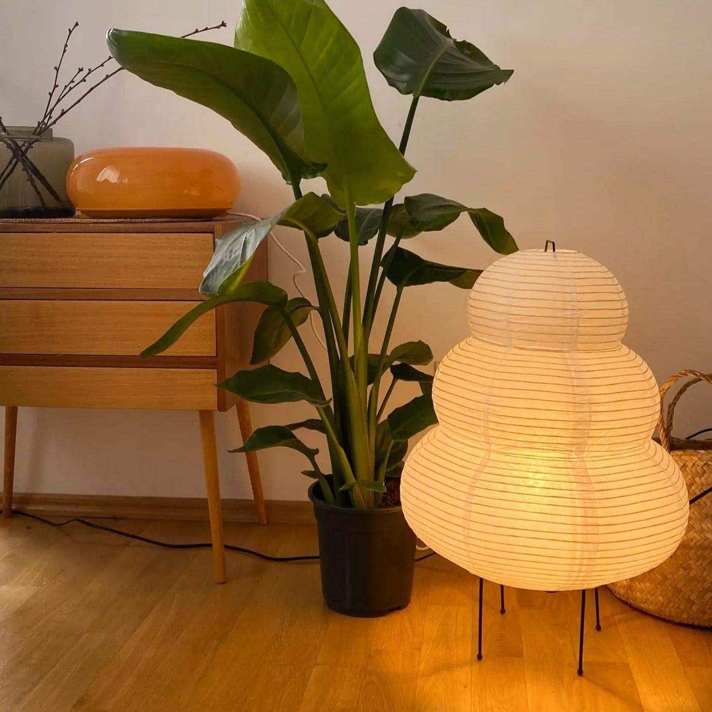 A warm glowing japanese hikaru lamp with rice paper shade and thin vertical lines on an iron tripod base