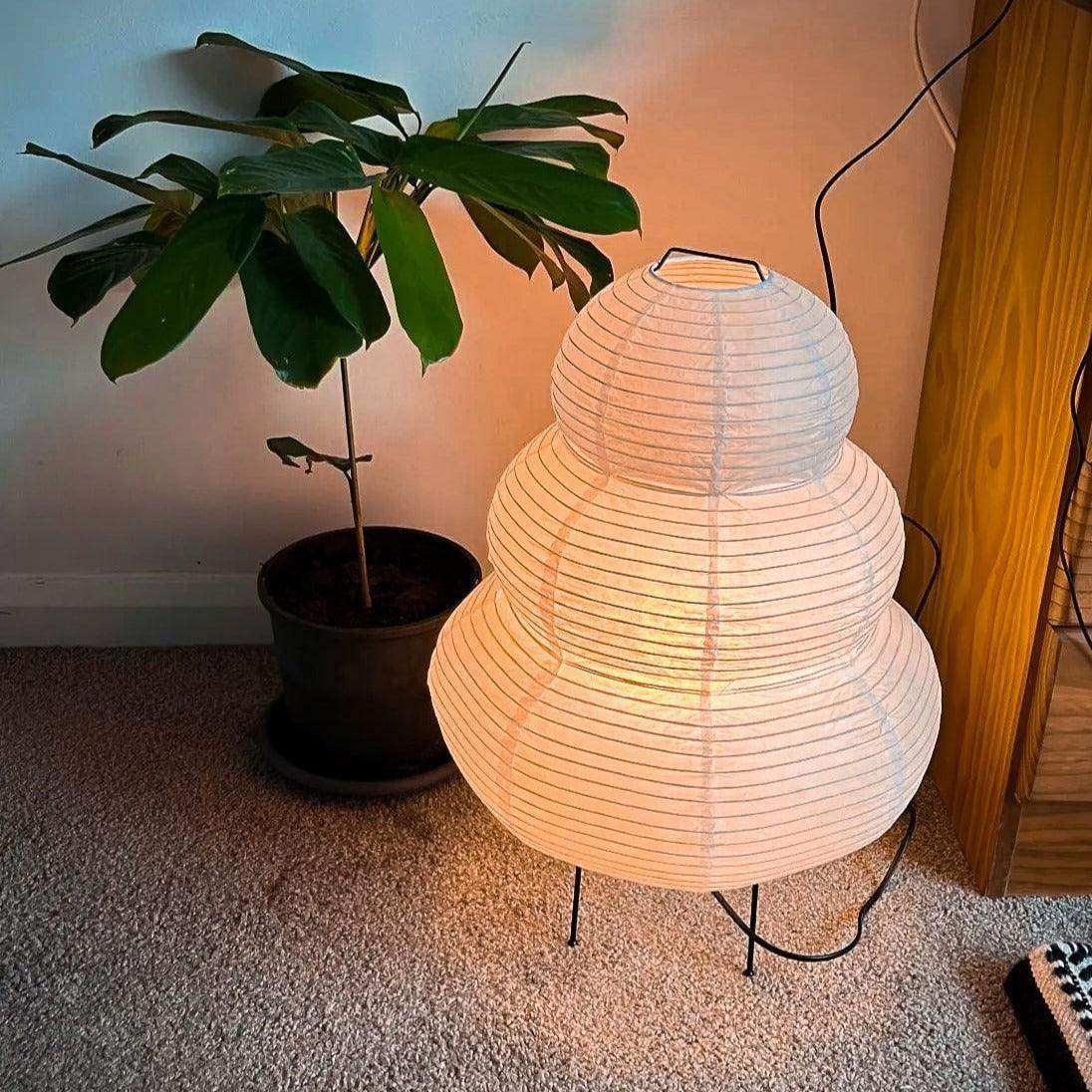 The japanese hikaru lamp is a warm white rice paper lamp with a tiered design and black iron tripod legs
