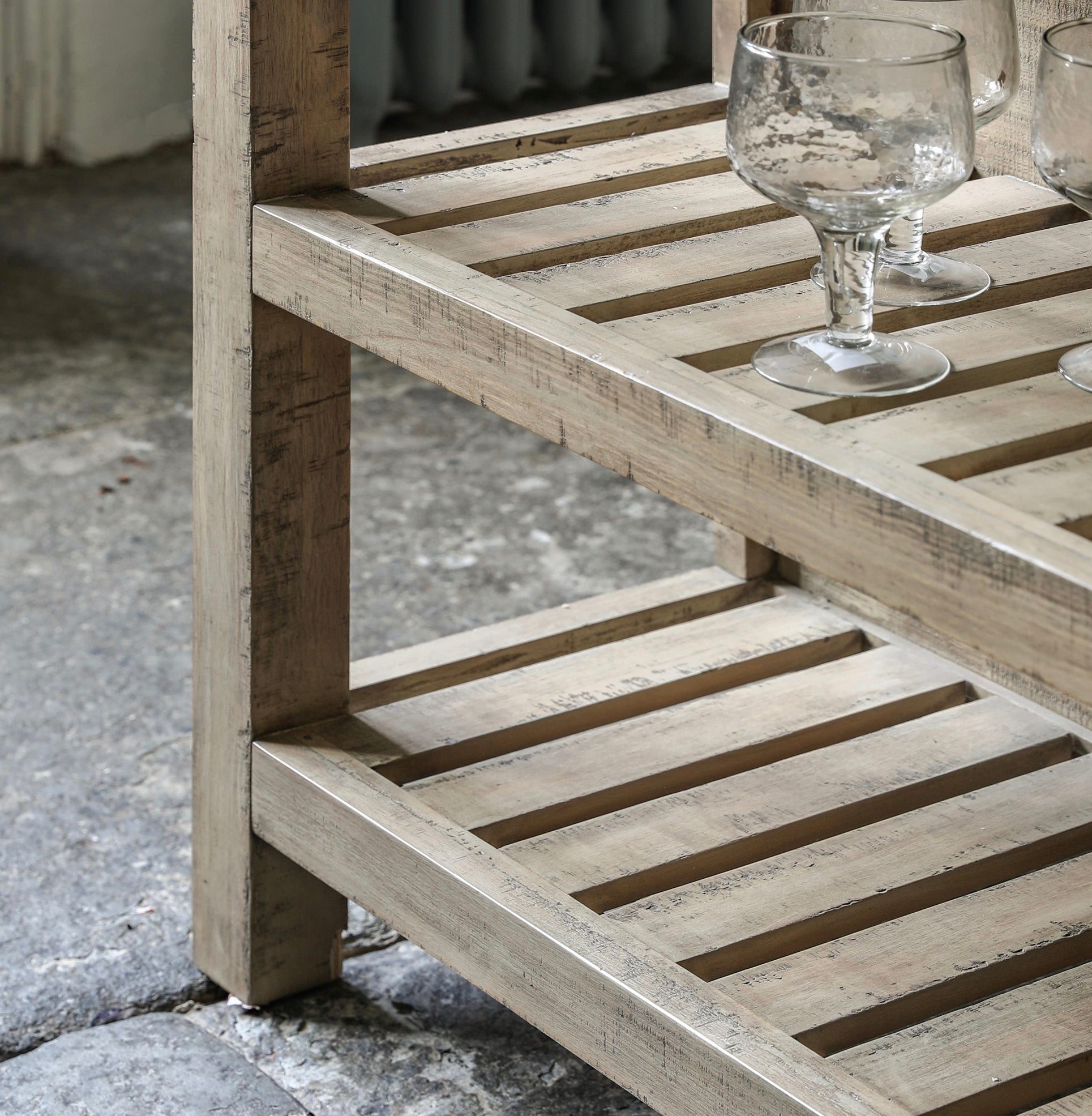 A rustic light gray wooden kitchen island side table with slatted shelves and a weathered finish