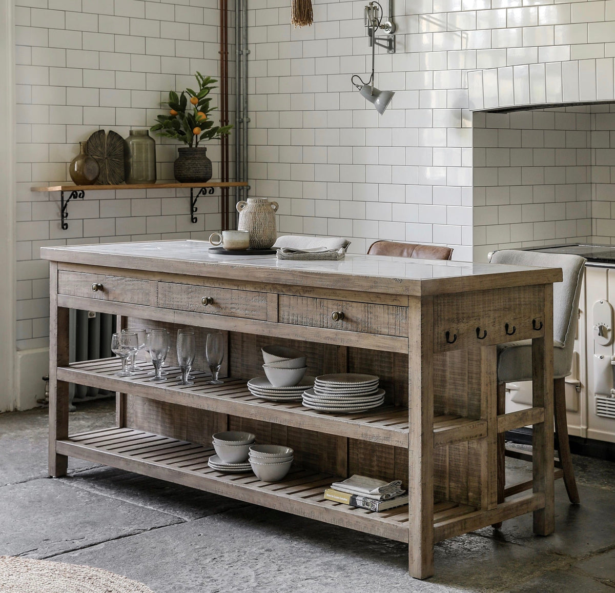 Rustic wooden manor kitchen island with light gray stone countertop, three drawers, and open shelving for storage