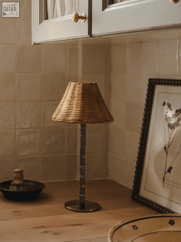 The raffles lamp features a woven wicker lampshade with a slender dark metal stem and solid brass base, made from responsibly sourced bamboo