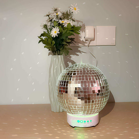 A rotating disco ball diffuser with a spherical mirrored design, pink base, and glowing green lights