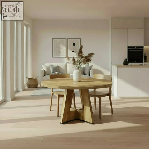 The somerset round oak dining table features a light wood pedestal base with a vase of dried pampas grass on top