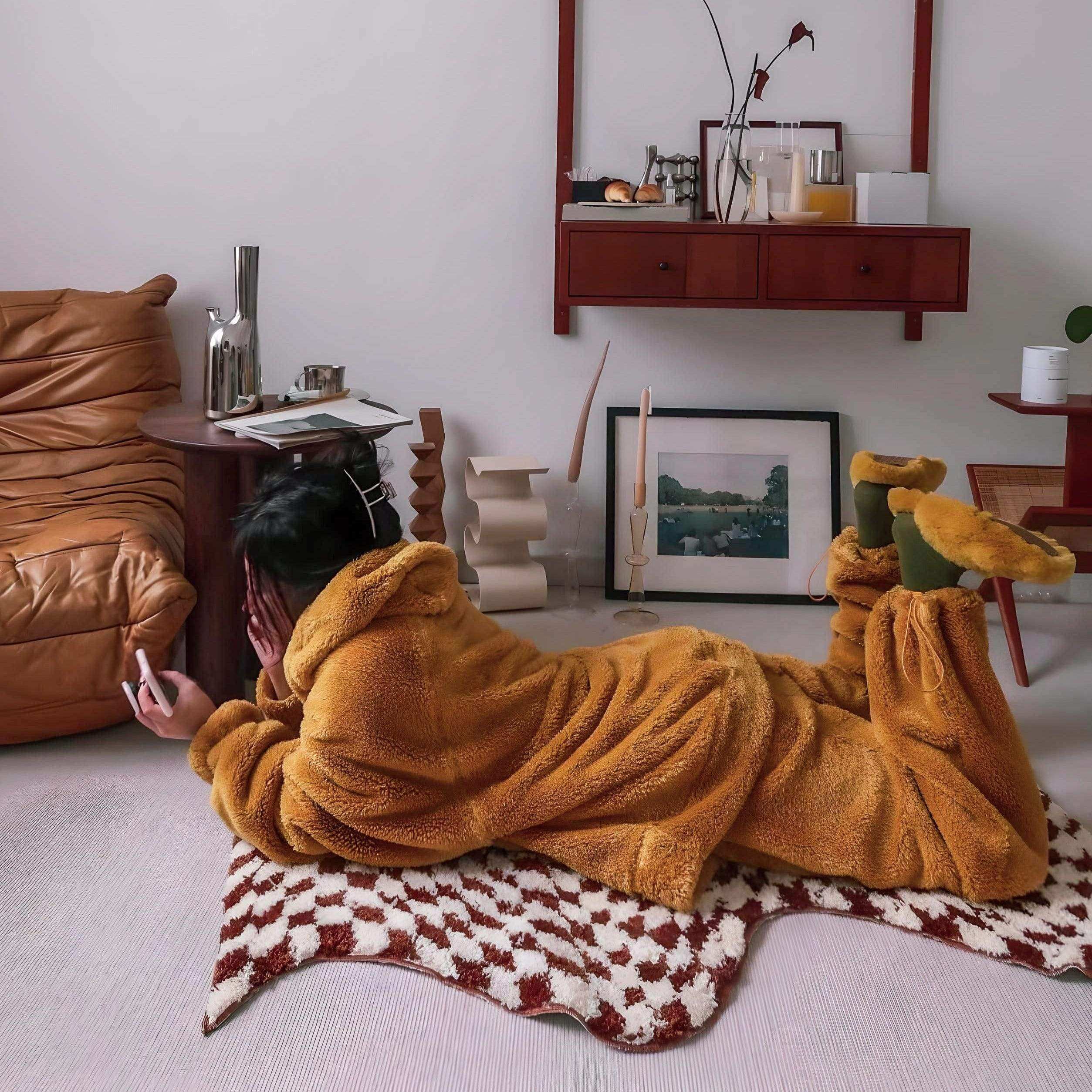 A cozy mustard-yellow plush pajama set with hood and fleece material on a wavy checkerboard rug