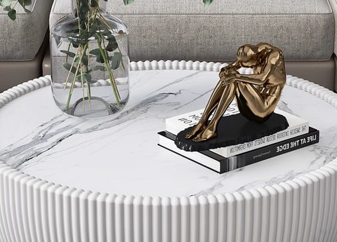 Golden metallic sculpture of seated figure on black base atop books as decorative accent for theo coffee table set black