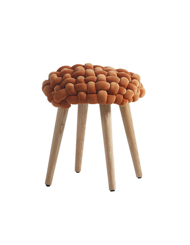 A cozy rust-colored thick knot dressing table stool with a knitted seat and slim wooden legs