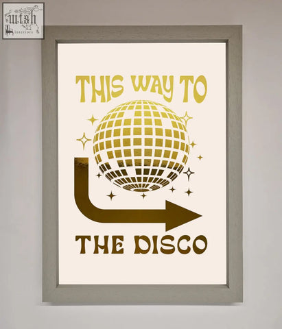 A framed poster with a gold disco foil print disco ball and arrow on an off-white background for party decor