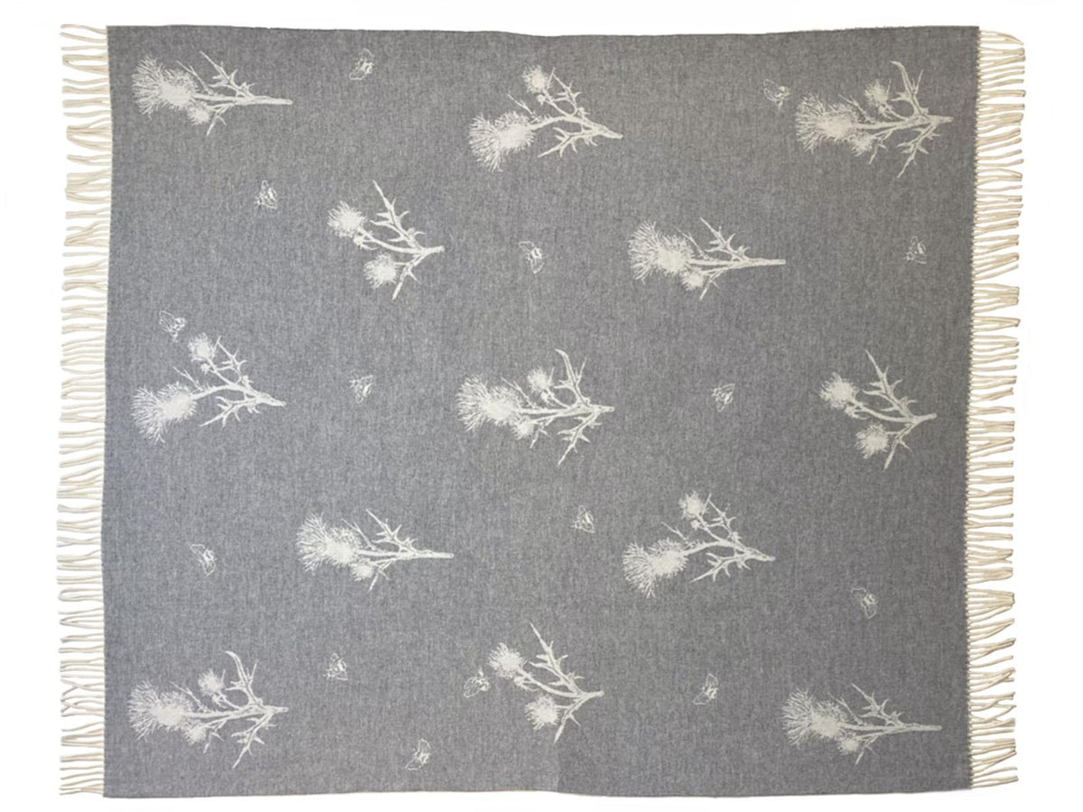 Gray merino lambswool throw blanket with white thistle and bee patterns and fringed edges for cozy use