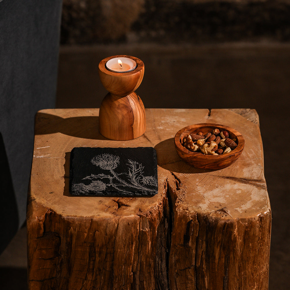 A warm-toned olive wood candle holder with a smooth finish paired with a thistle trio single slate coaster
