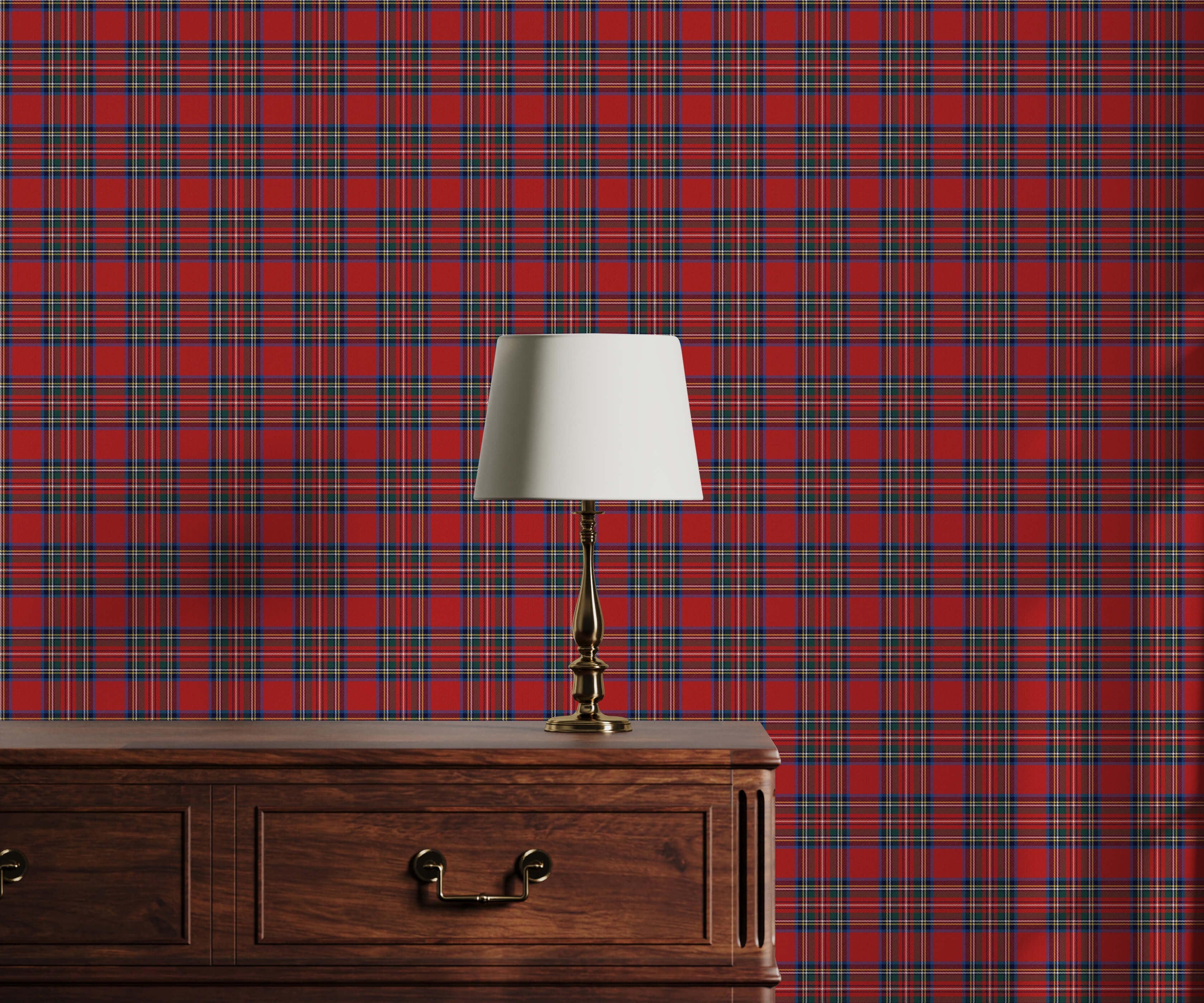 A classic brass thompson table lamp with a white tapered shade on a dark wood dresser by tartan wallpaper