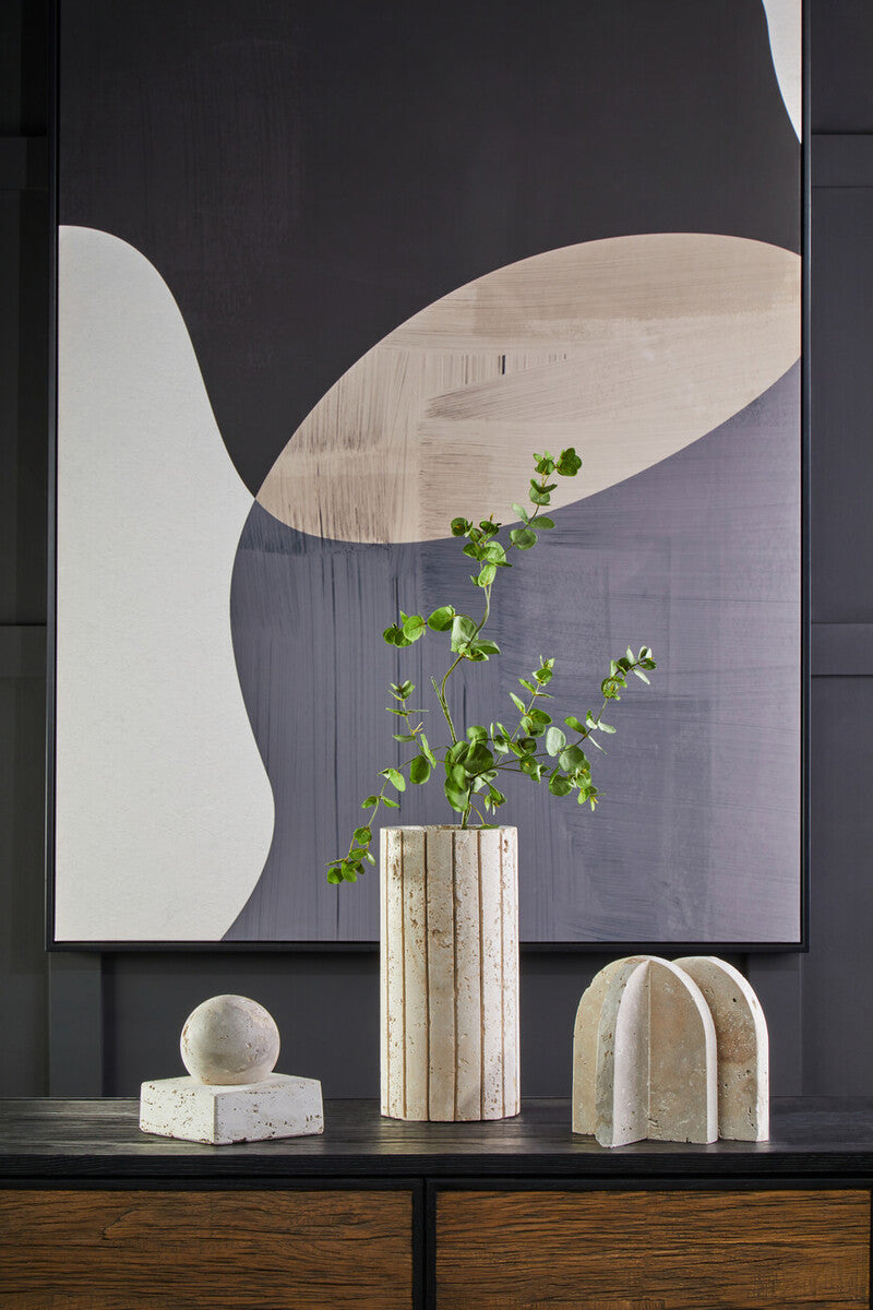 A tall tibor travertine ribbed vase with vertical grooves and an off-white finish holding delicate green foliage