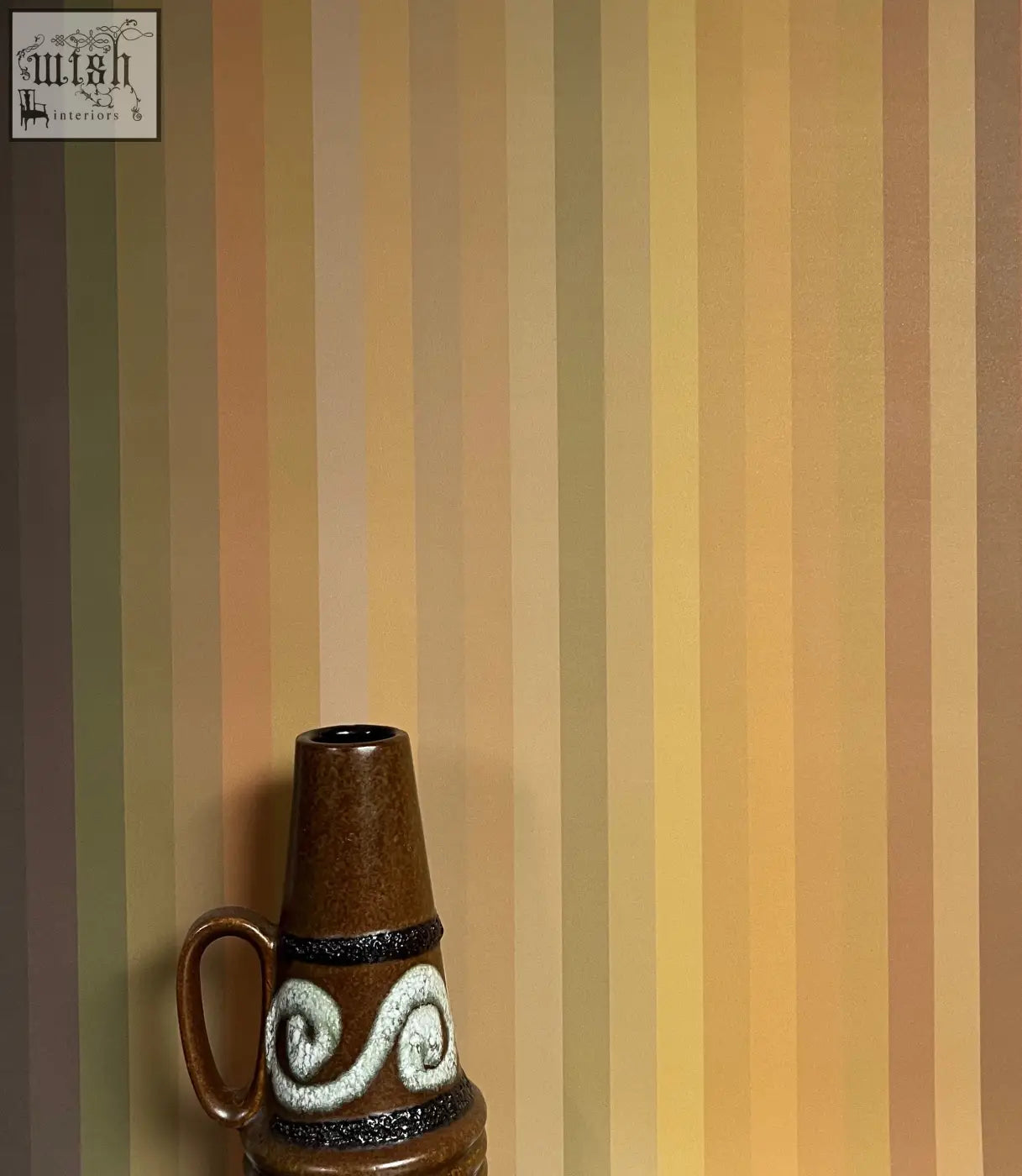 Brown ceramic vase with white swirls and black bands complementing tonal stripe wallpaper ochre colour ways