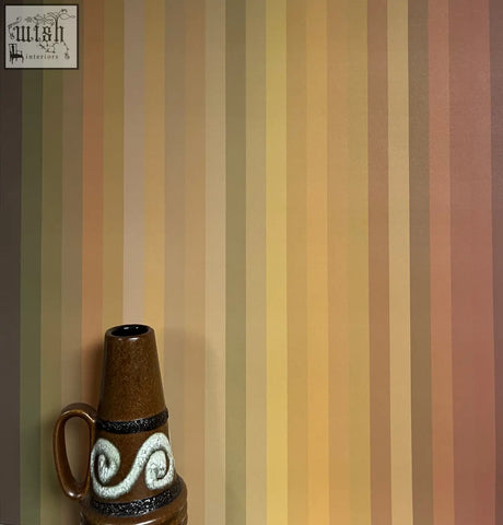 Brown ceramic vase with white swirls and black bands complements tonal stripe wallpaper ochre colour ways design