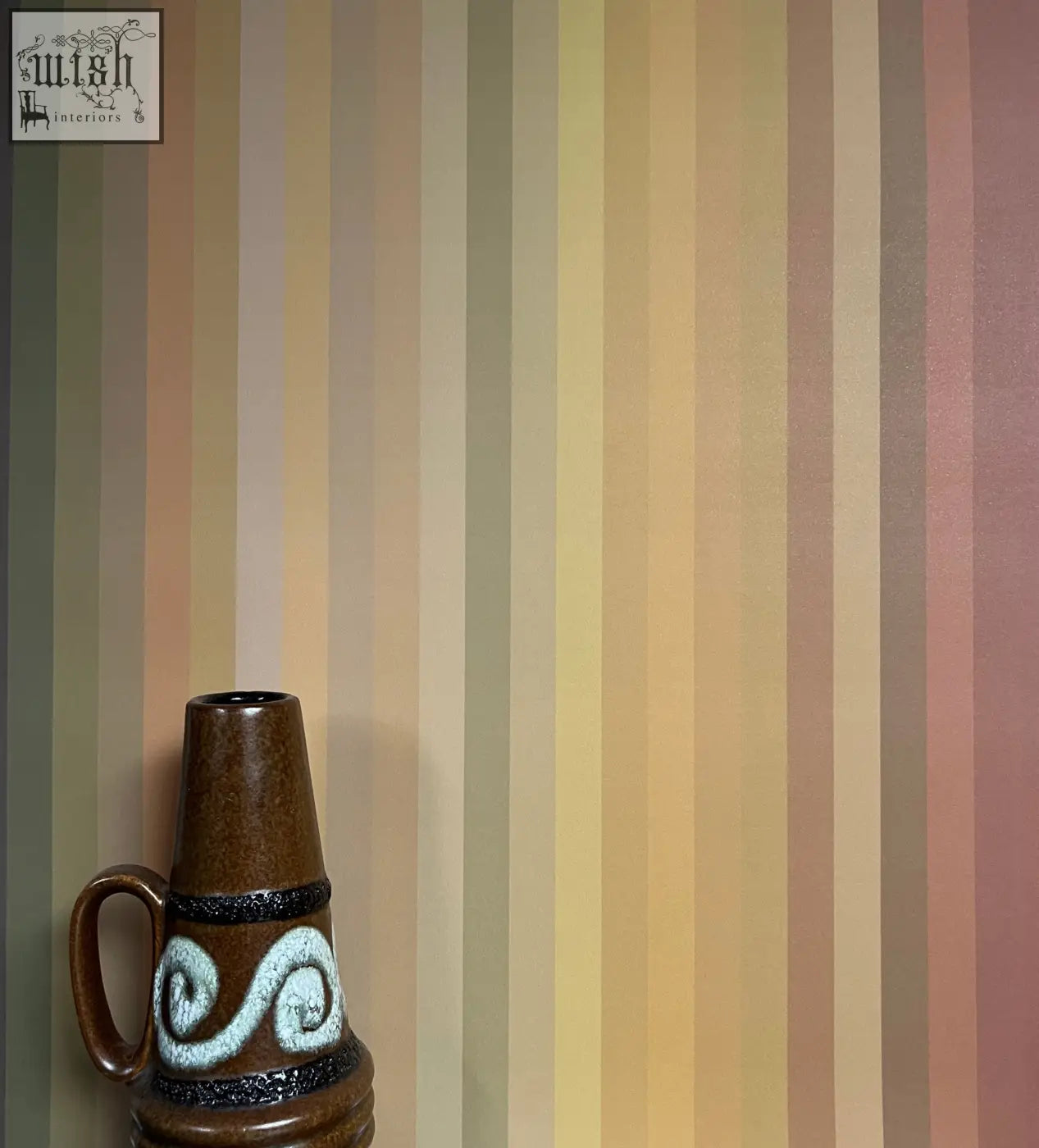 Brown ceramic vase with handle and white swirling pattern shown against tonal stripe wallpaper ochre color ways background