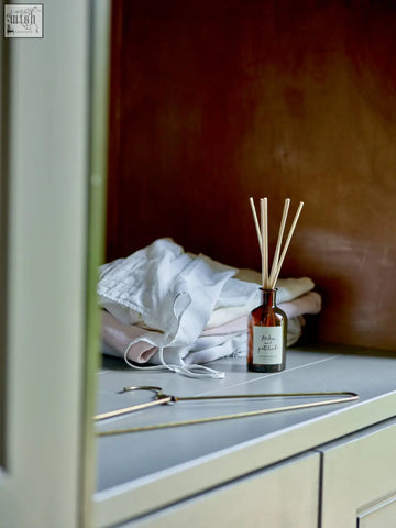 Amber glass reed diffuser with minimalist white label and wooden reeds offering consistent fragrance throw of tonka bean and woody patchouli
