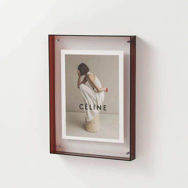 A sleek dark wood-framed wall-mounted transparent acrylic picture frame showcasing a celine advertisement poster