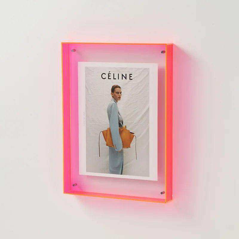 A vibrant pink transparent acrylic picture frame holding a celine magazine cover with an orange leather handbag