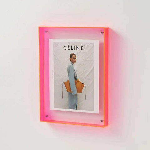 A vibrant pink transparent acrylic picture frame holding a celine magazine cover with an orange leather handbag