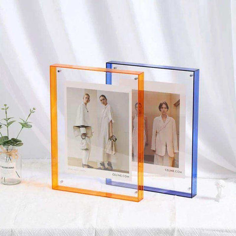 Two transparent acrylic picture frames with orange and blue borders holding fashion magazine pages displayed upright