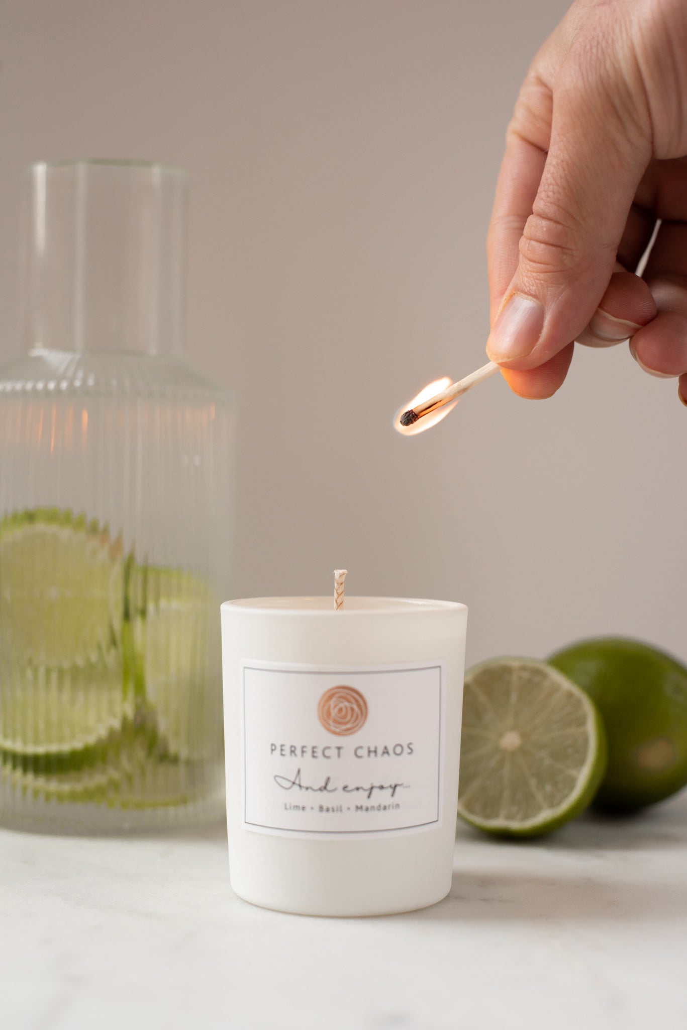 White cylindrical travel candle with minimalist perfect chaos label and circular logo set against lime slices
