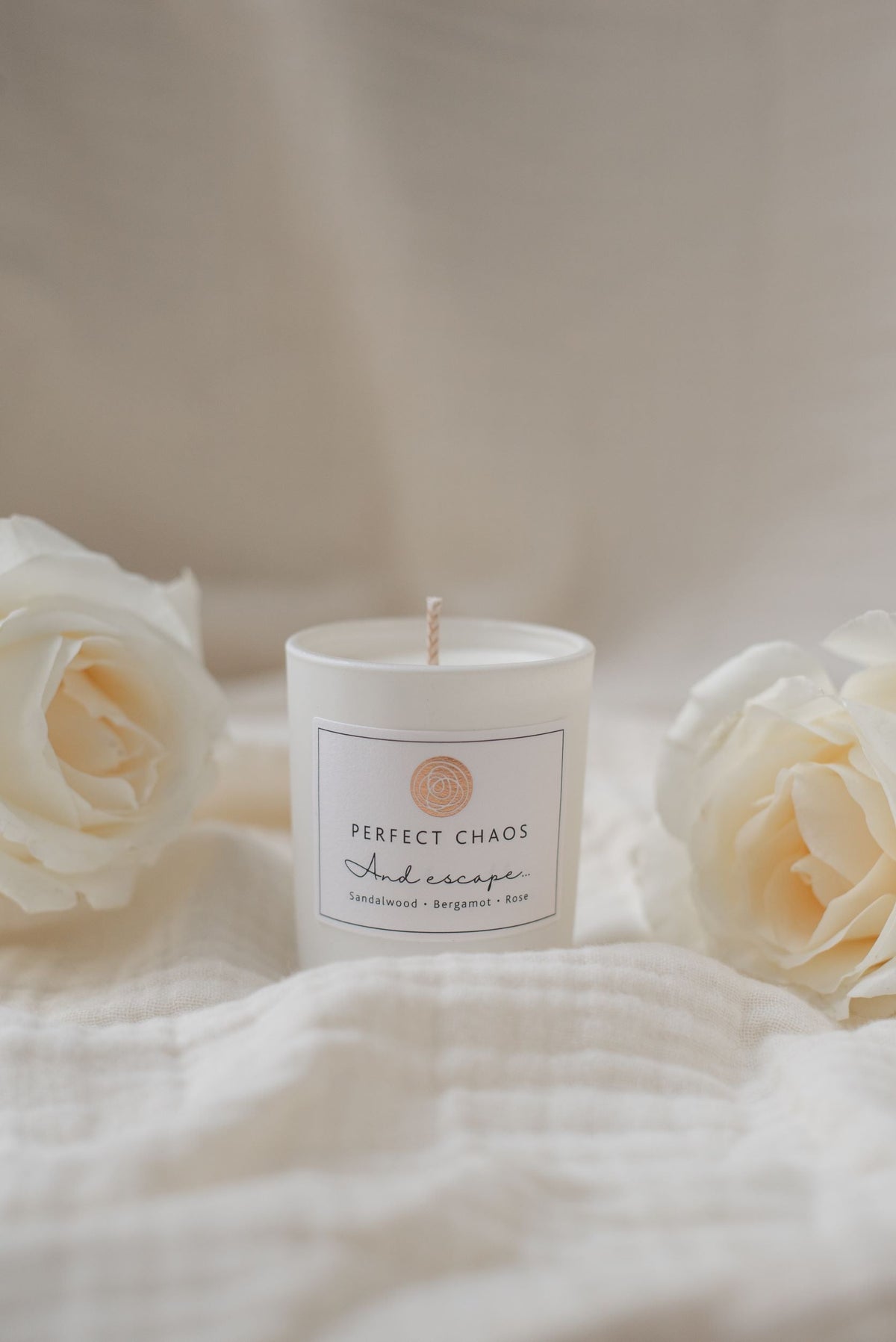 A white cylindrical travel candle labeled perfect chaos and escape with sandalwood bergamot and rose scent