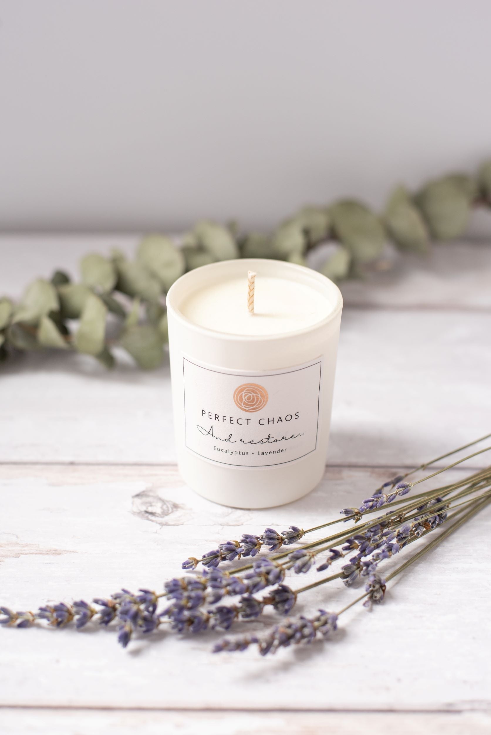 A white cylindrical travel candle with perfect chaos and restore label featuring eucalyptus lavender essential oils scent