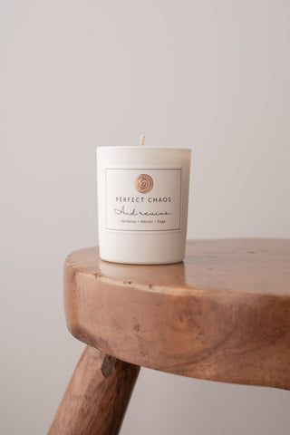 A minimalist white travel candle in a glass jar labeled perfect chaos with essential oils for revive moods