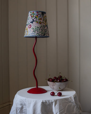A vibrant red sinuous metal lamp base with a tree of life lampshade featuring colorful floral and bird motifs