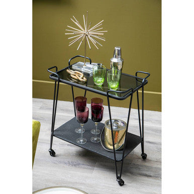 Black metal trento bar trolley with glass shelves and wheels holding green cocktail shakers and red wine glasses