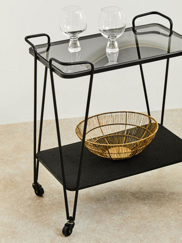 Black metal trento bar trolley with grey glass top and lower shelf, featuring a gold wire basket on the bottom