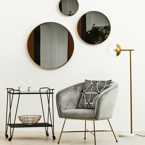 Gray velvet armchair with gold-tone metal legs and black-and-white pillow next to trento bar trolley with grey glass shelves